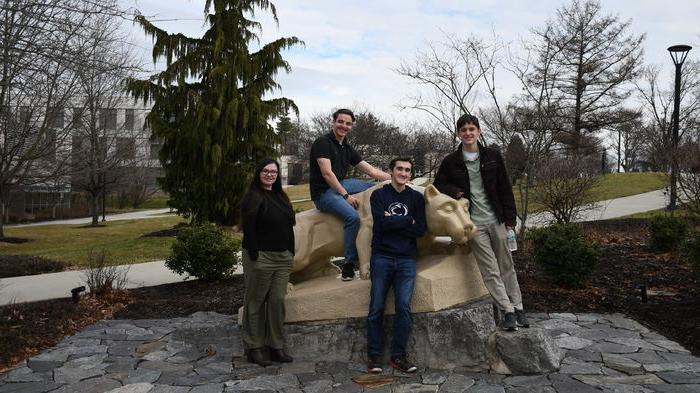 Four male students pose for picture on Nittany Lion statue