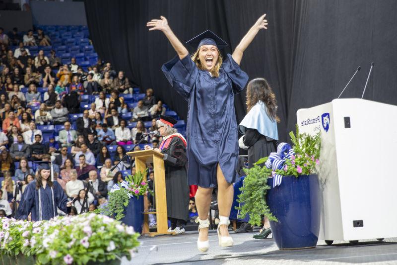 毕业典礼上，一名学生戴着礼帽，穿着长袍，兴高采烈地跳着穿过舞台